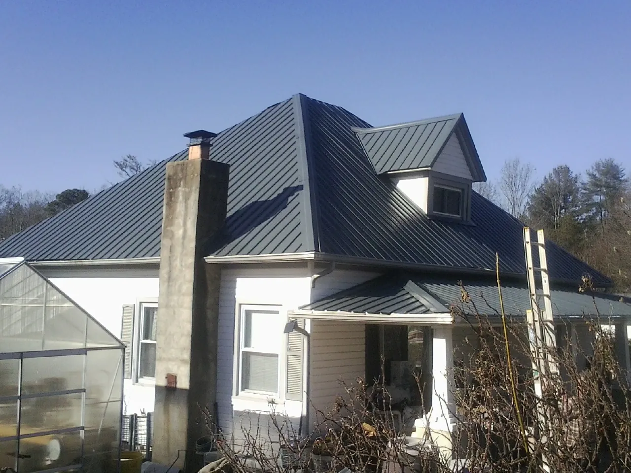 Dark blue standing seam metal roof on a white farmhouse with dormer — Slate & Tile Roof Repair by Roofing Brothers in Lyons