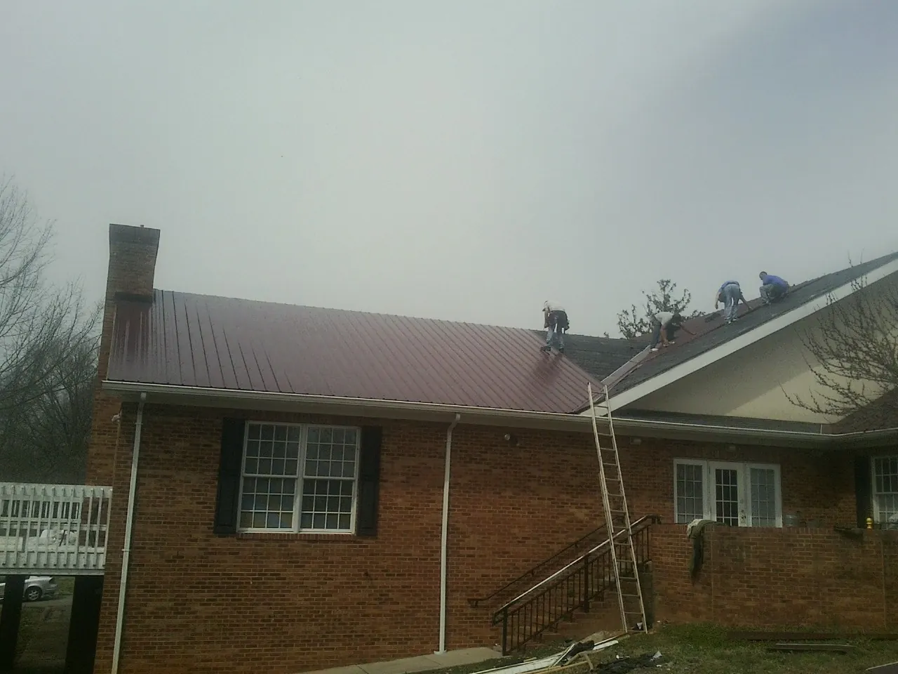 Crew setting red metal roofing panels on a brick home in Lyons