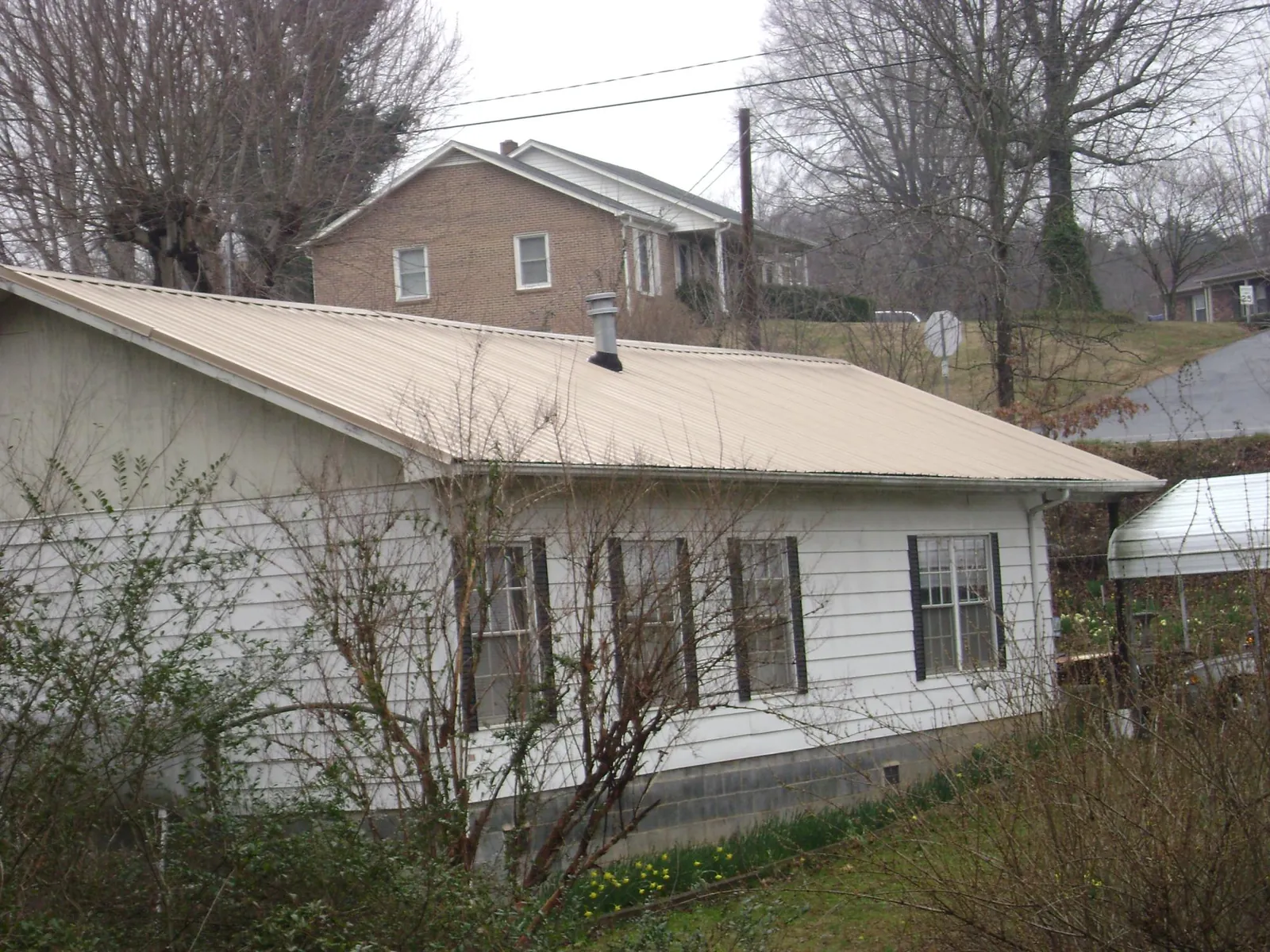 Tan metal roof on a white sided house set into a hillside — Commercial Roofing by Roofing Brothers in Lyons